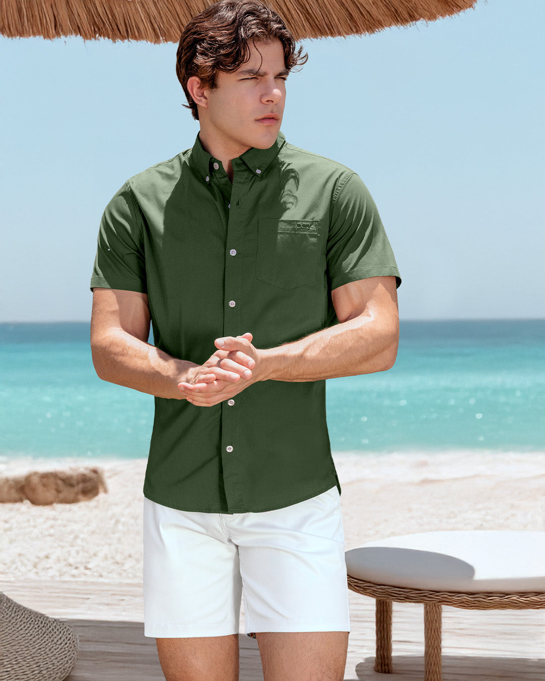 DC2 Alpha Green Cotton Shirt and White Street Shorts — model standing under a straw umbrella at the beach, wearing a fitted button-down shirt in deep green paired with crisp white shorts for a clean, elevated summer look.