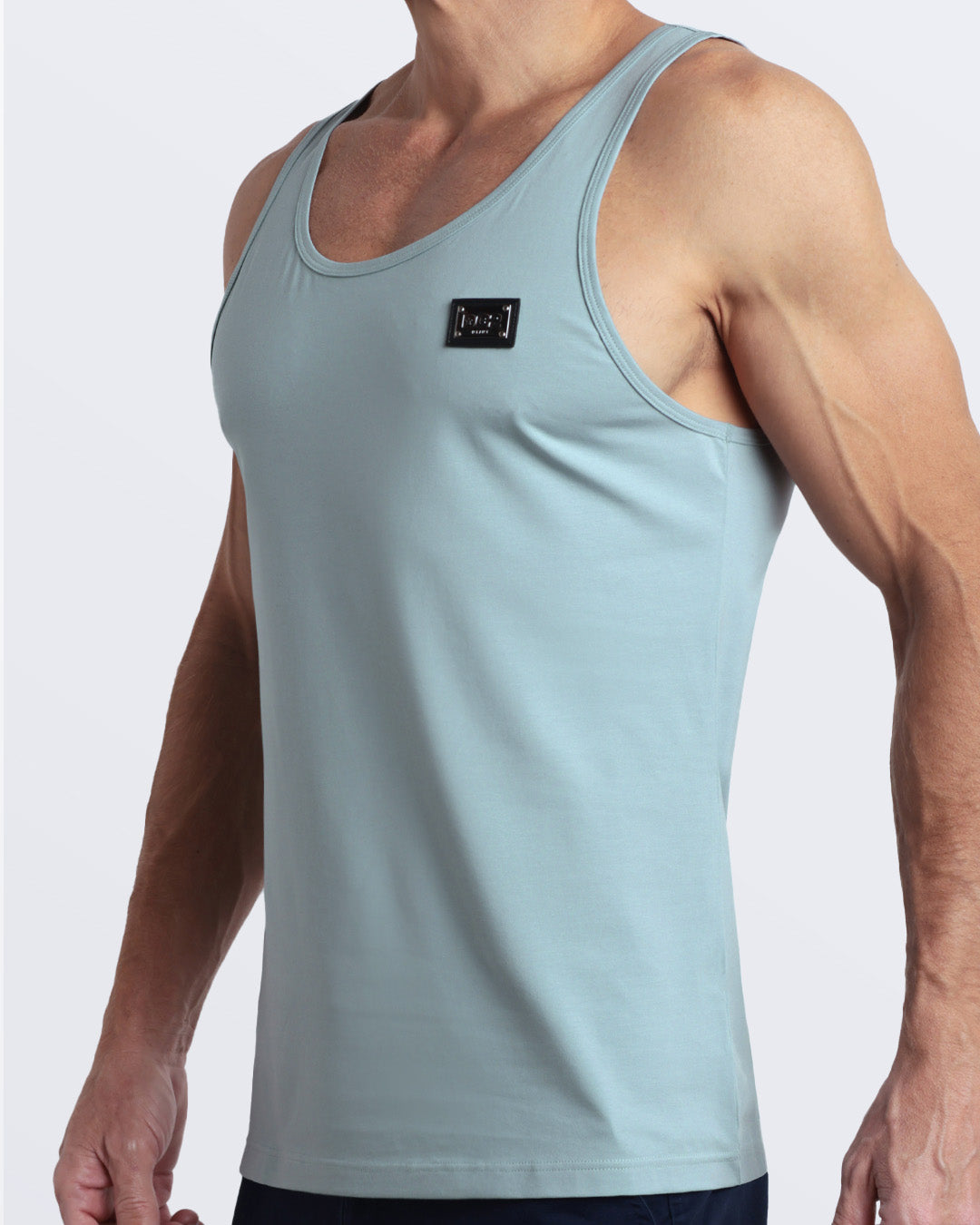 Side view of men’s workout tank top in BARELY TEAL a soft, muted teal shade color with a metallic plaque logo made by DC2 Clothing the new official brand of mens beachwear.