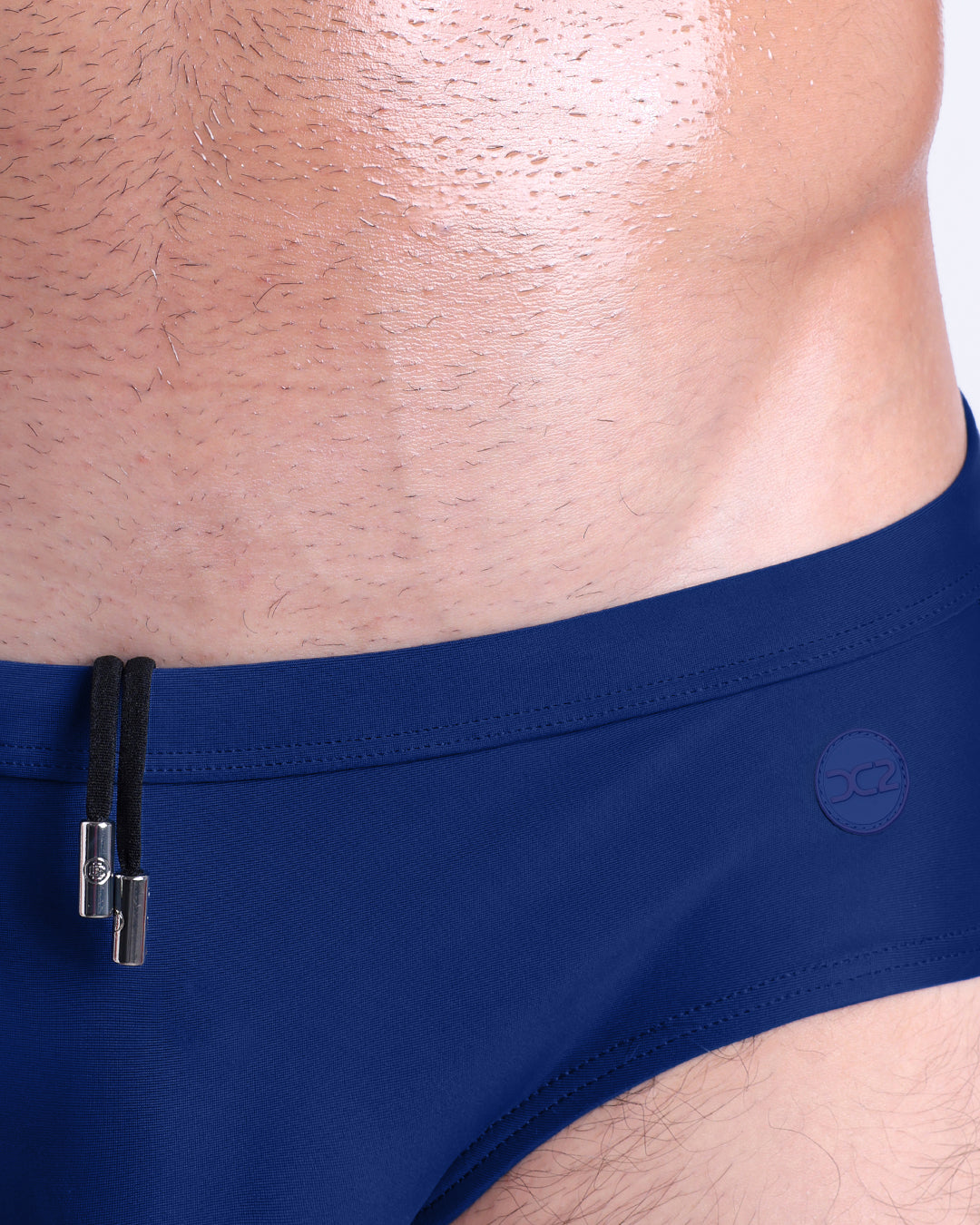 Close-up of BLUE BY THE OCEAN swim briefs — adjustable drawstring detail with metal tips and tonal logo.