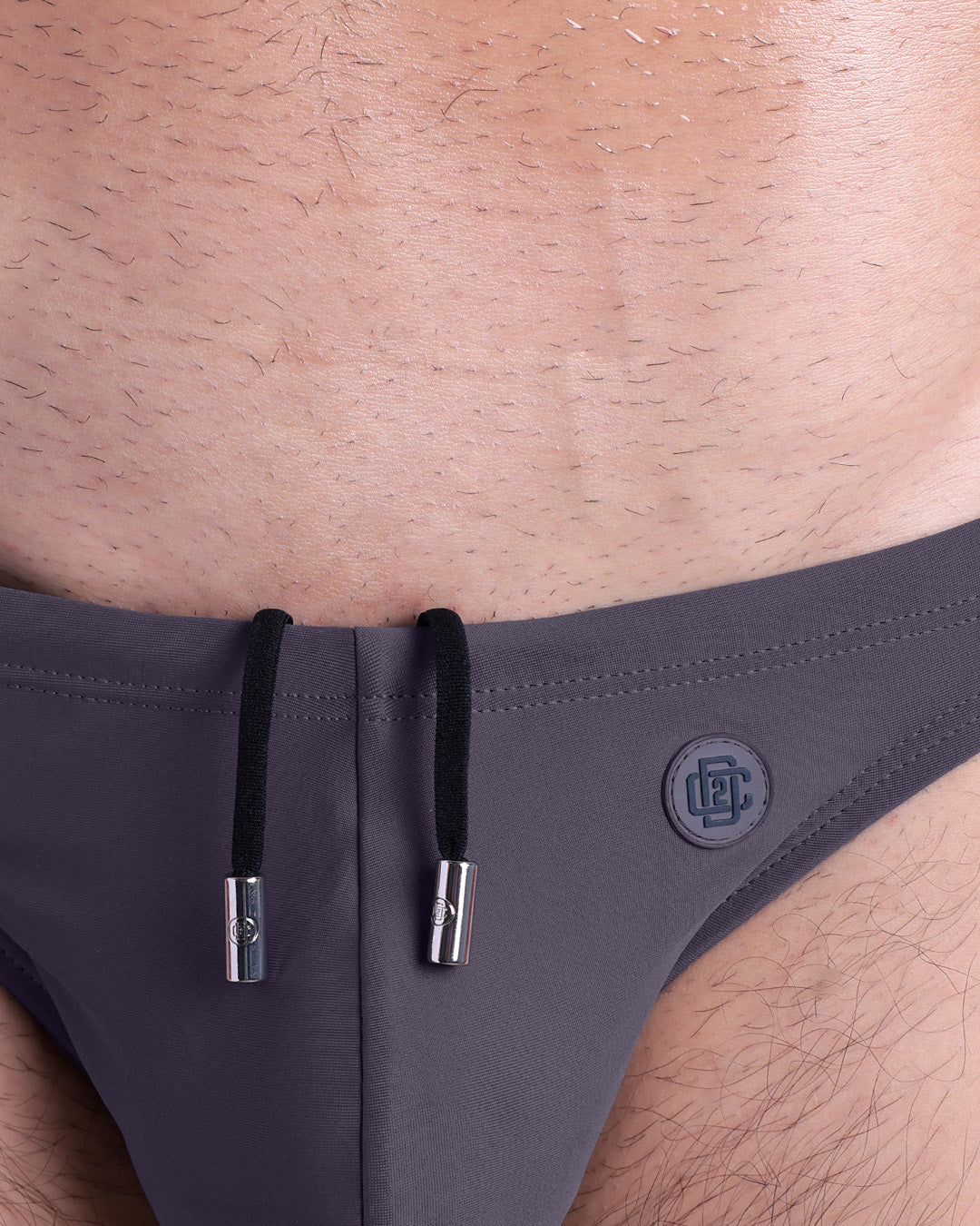 Close-up view of the GOTHAM GREY men’s drawstring briefs showing black cord with custom branded metallic silver cord ends, and matching custom eyelet trims in silver.