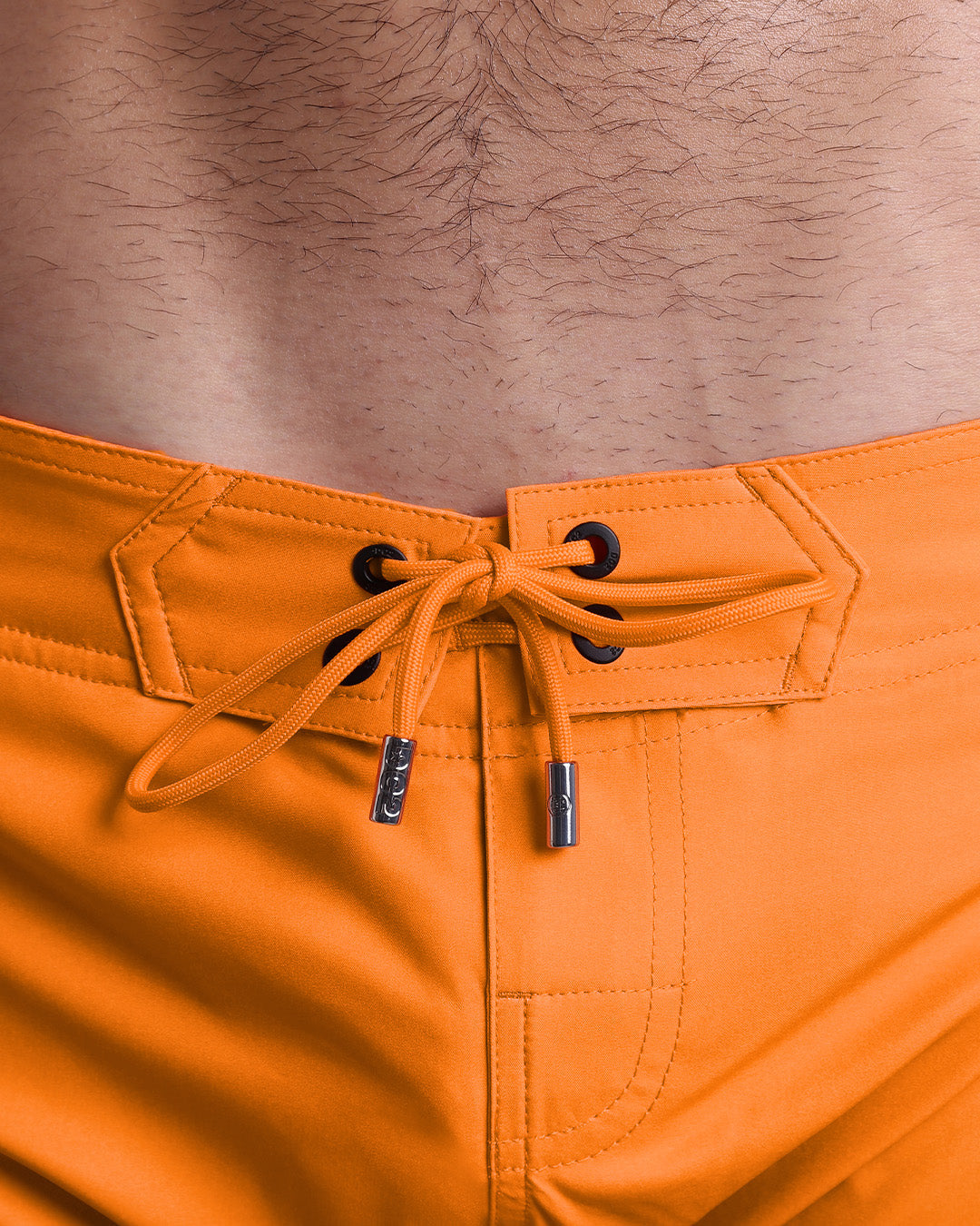Close-up view of inseam and details of MATCH POINT ORANGE beach shorts for men, with a orange color cord and custom branded silver cord-ends, and matching custom eyelet trims in black.