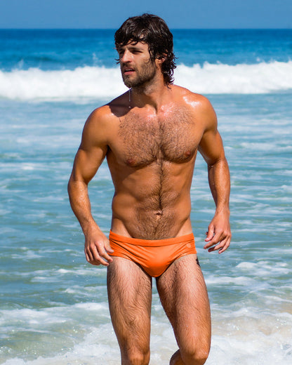 Man emerging from the ocean in bright orange Swim Briefs from DC2 Miami. Bold and vibrant men’s swimwear designed for a perfect fit and style. Shop DC2 Miami’s premium swim collection for men’s beachwear.