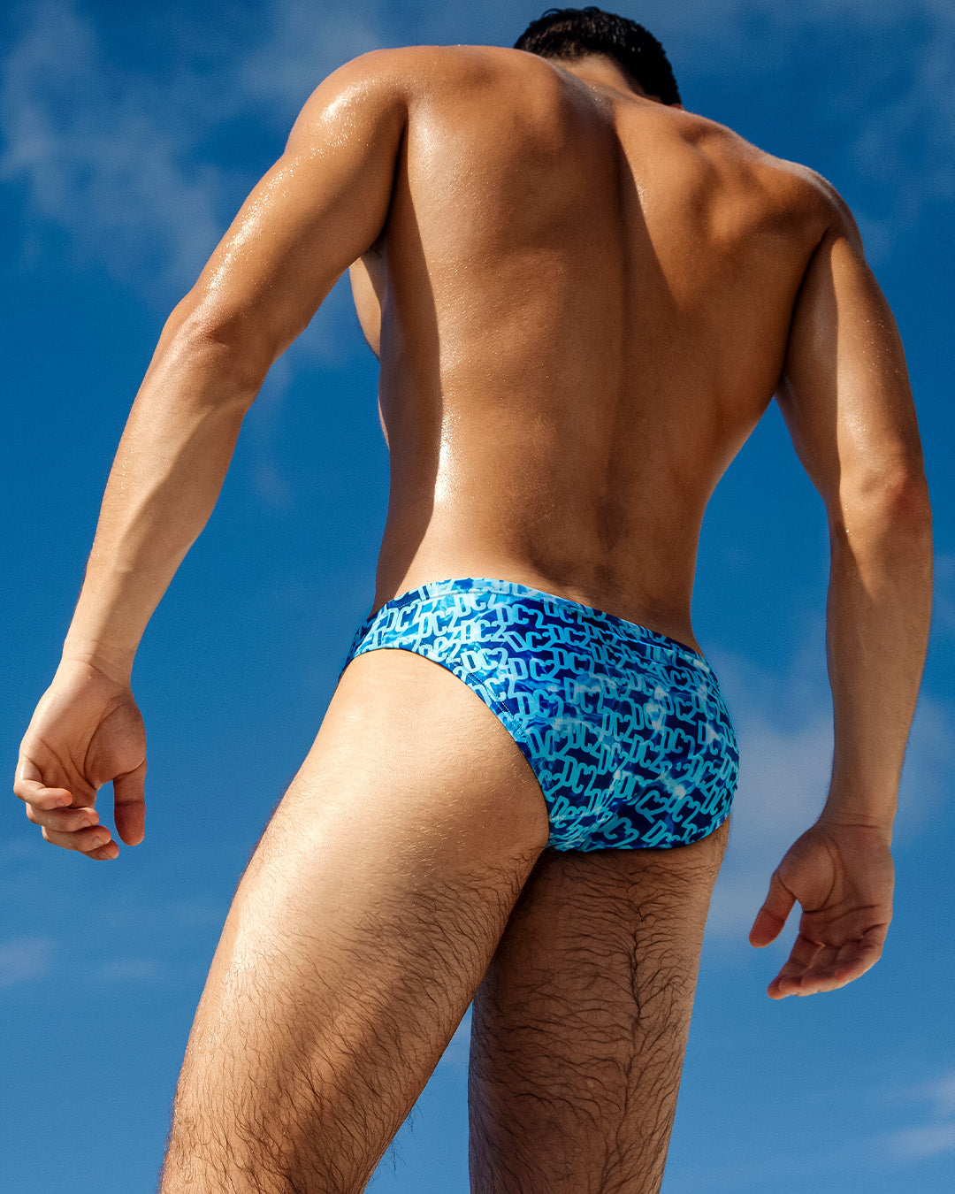 Back view of a model wearing DC2 Miami WET Swim Mini Briefs, showcasing the bold blue gradient design with DC2 branding.