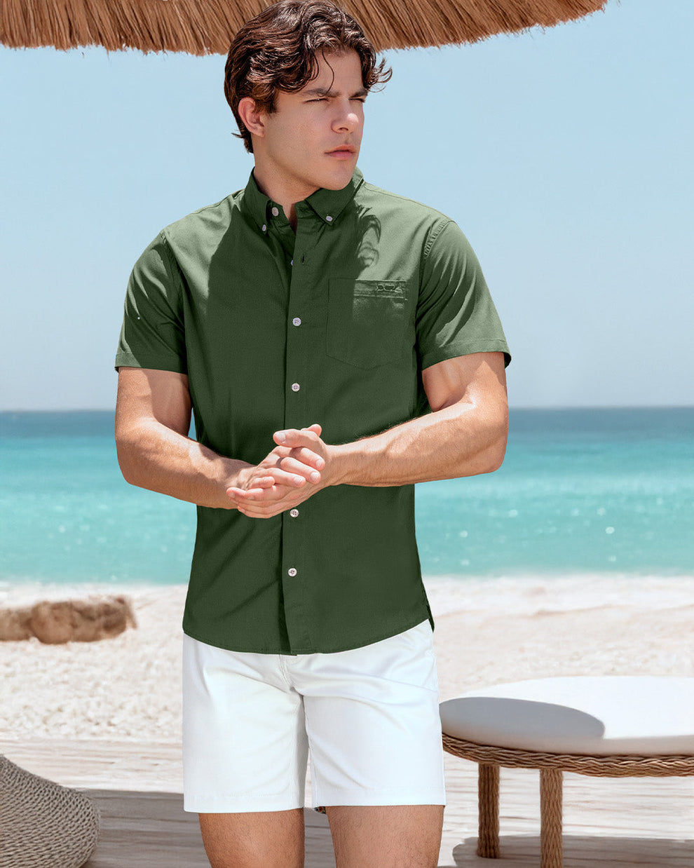 DC2 Alpha Green Cotton Shirt and White Street Shorts — model standing under a straw umbrella at the beach, wearing a fitted button-down shirt in deep green paired with crisp white shorts for a clean, elevated summer look.