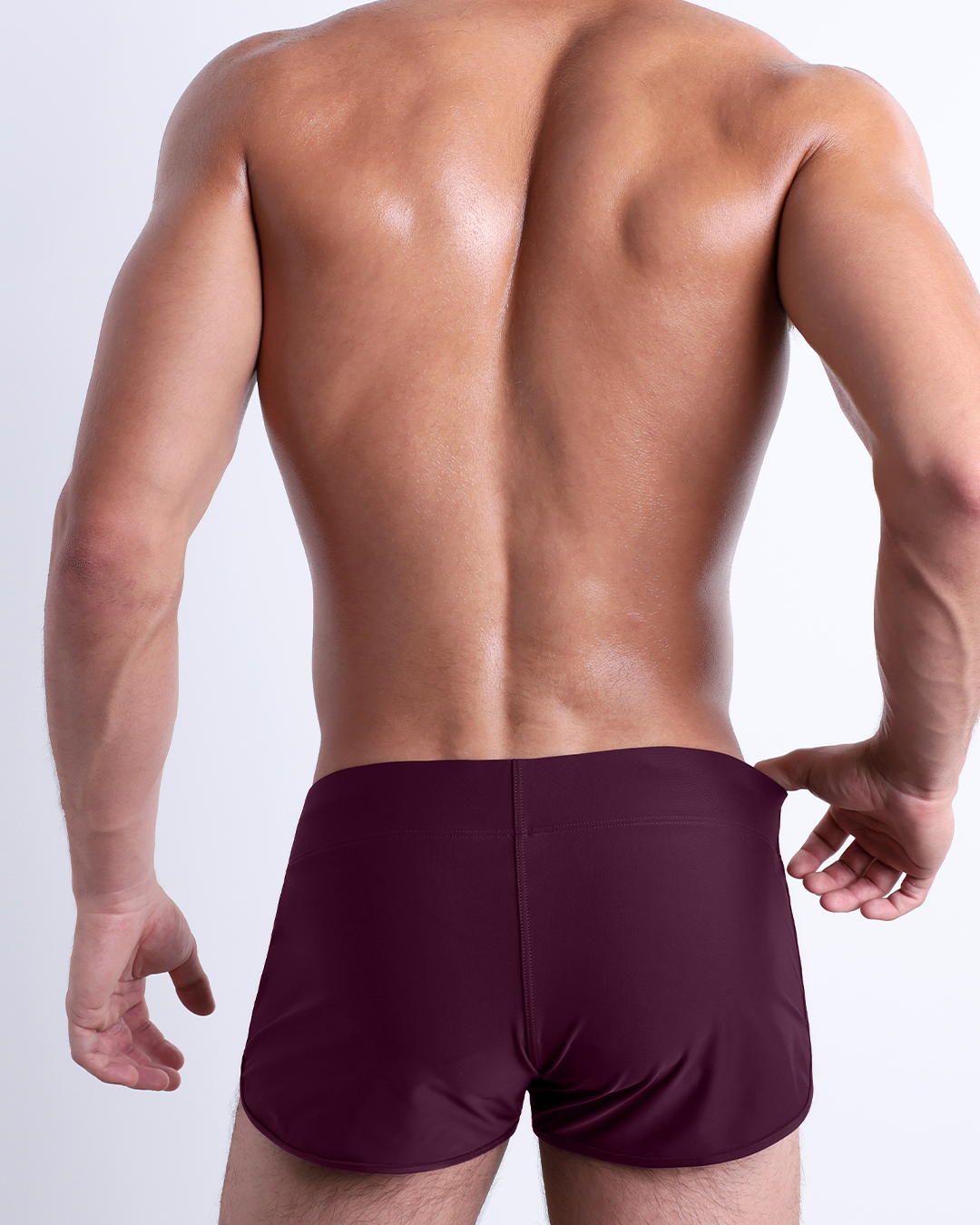 Back view of a male model wearing the BERRY GOOD beach Swim Shorts for men by BANG! Miami in a solid red wine color.