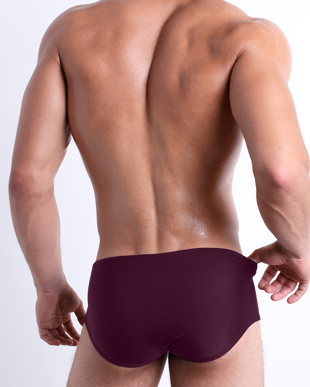 Back view of a male model wearing the BERRY GOOD beach Brazilian Sunga swimwear for men by BANG! Miami in a solid red wine color.