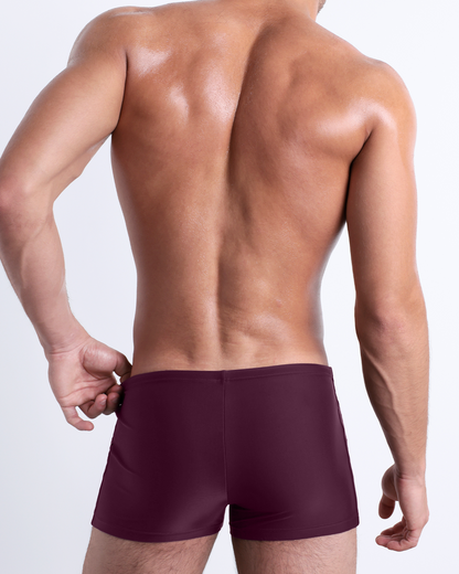 Back view of a male model wearing the BERRY GOOD men’s swim trunks by DC2 Miami in a solid wine-red color.