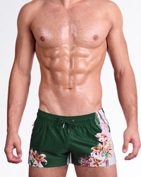 DC2 Bloom Service Poolside Shorts — model wearing dark green poolside swim shorts featuring a bold tropical floral print with lily-inspired blooms, adjustable drawstring waistband, and modern short-length beach fit.