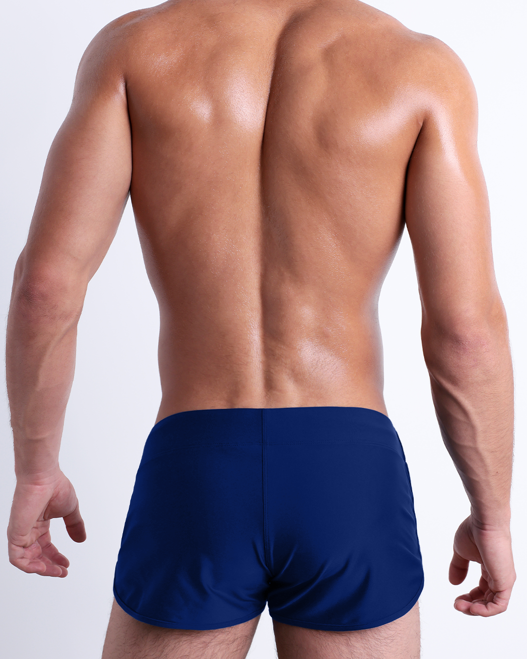 Back view of a male model wearing the BLUE BY THE OCEAN beach Swim Shorts for men by DC2 Miami in a solid dark blue color.