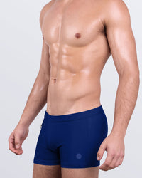 DC2 Blue by the Ocean — model wearing Blue by the Ocean Swim Trunks featuring rich deep navy tone and sleek square-cut silhouette.