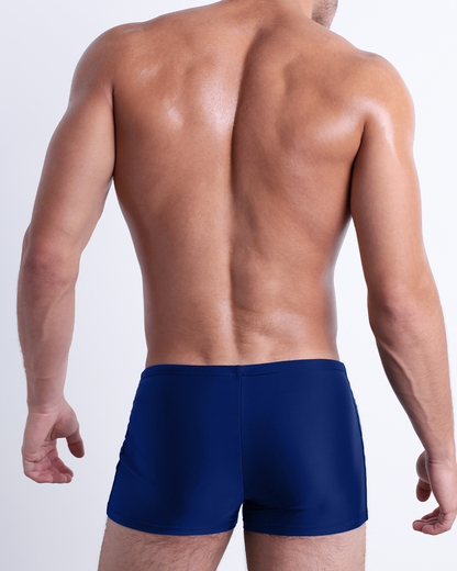 Back view of a male model wearing the BLUE BY THE OCEAN men’s swim trunks by DC2 Miami in a solid vibrant blue color.