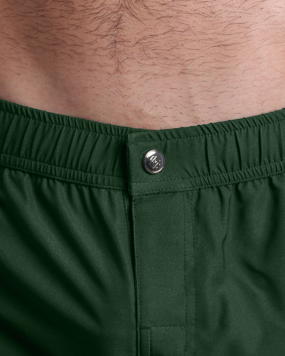 Close-up view of the BRAVE GREEN men’s swimwear, showing custom branded silver metal logo.