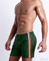 Side view of the BRAVE GREEN for men’s summer Resort Shorts with dual zippered pockets in a solid green color with orange and white colored stripes on the side designed by DC2 a brand based in Miami.