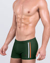 DC2 BRAVE GREEN Swim Trunks — model wearing square-cut men's swim trunks featuring bold white and orange racing stripes.