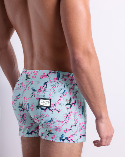 Side view of the CLOSE TO YOU men’s summer Beach Shorts, with dual zippered pockets. The shorts have a stylish exotic birds design in a light blue color with pink flowers for men. These high-quality swimwear bottoms by DC2, a men’s beachwear brand from Miami.