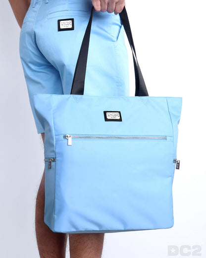 Side view of the COASTAL BLUE Poolside Tote Bag Foldable/Portable by DC2 brand. Features smooth zipper in the front and the side, water resistant fabric, and the DC2 logo in a metallic silver plaque.