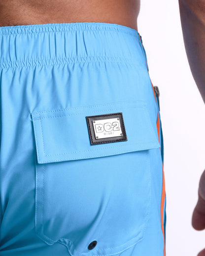 Close-up view of the COASTAL BLUE men’s Flex Boardshorts back pocket, showing custom branded silver metal logo.