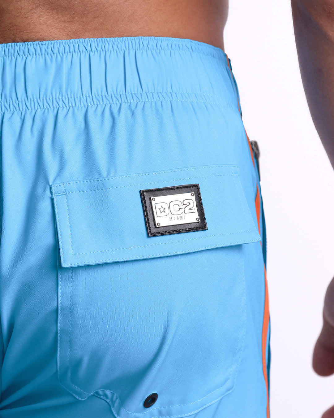 Close-up view of the COASTAL BLUE men’s Flex Shorts back pocket, showing custom branded silver metal logo.