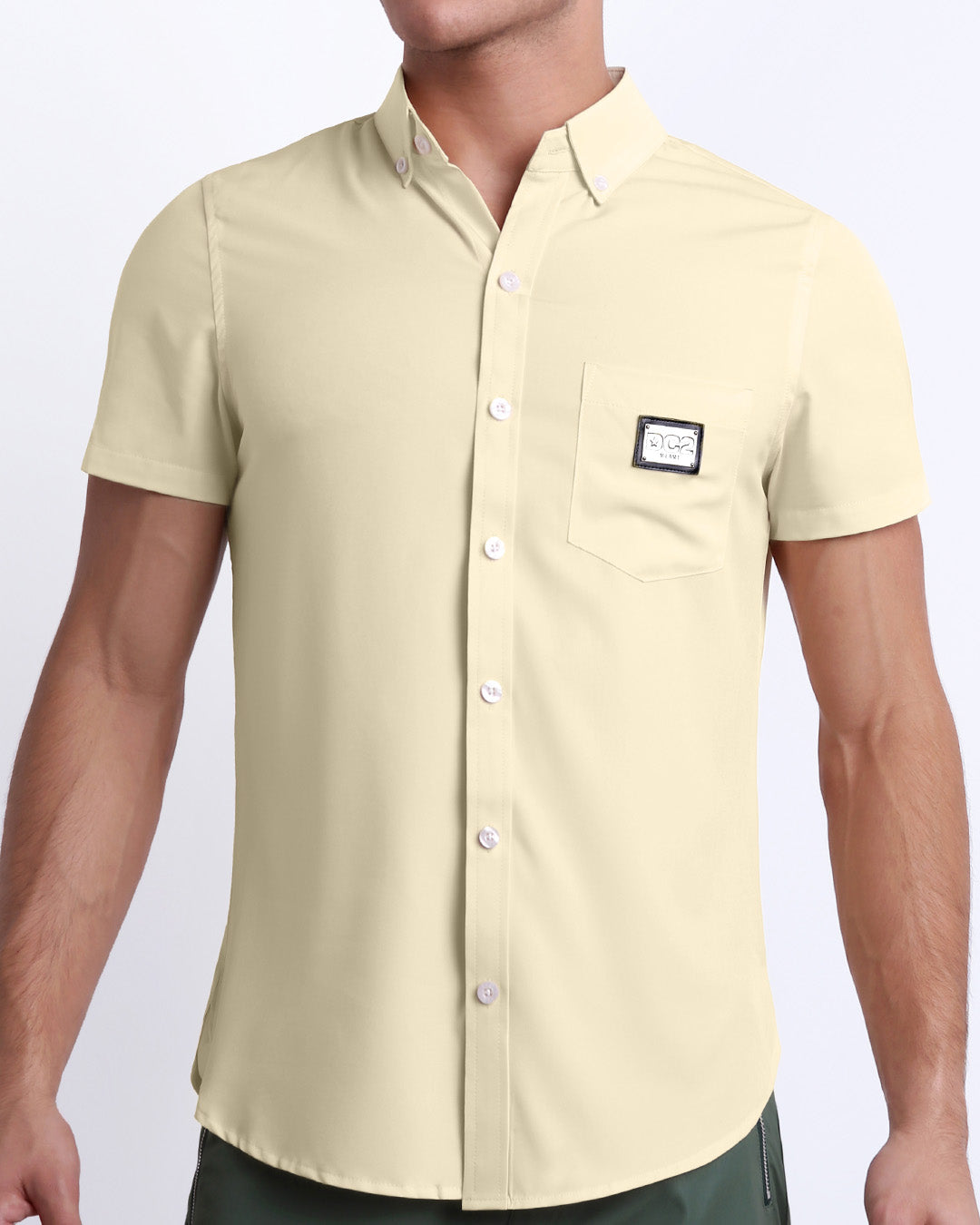 This is a front view of a male model looking sexy in a CREAM FIELDS stretch shirt for men. The shirt is a solid pale beige color on the left pocket. It's a premium quality button-up top made by DC2, a Miami-based men's beachwear brand.