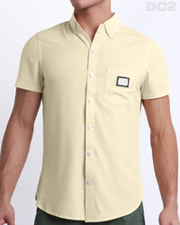 This is a front view of a male model looking sexy in a CREAM FIELDS stretch shirt for men. The shirt is a solid pale beige color on the left pocket. It's a premium quality button-up top made by DC2, a Miami-based men's beachwear brand.