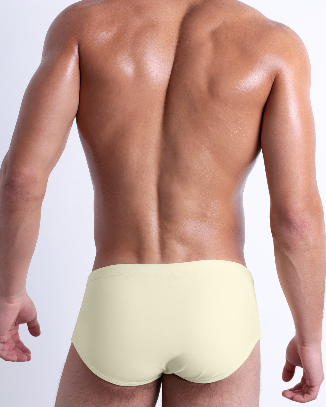 Back view of a male model wearing the CREAM FIELDS beach Brazilian Sunga swimwear for men by DC2 Miami in a solid light yellow color.