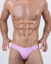 Model wearing FAST LINES (CHILL PINK) swim mini briefs for men featuring alternating pink and soft white vertical stripes. Bold, low-rise designer swimwear crafted to hug the waist and elevate beachwear with a sleek, vibrant edge.