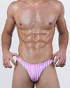 Male model wearing DC2 FAST LINES (CHILL PINK) swim thong with vertical pink and white stripes, low-rise cut for sleek tan lines.