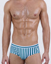 Model wearing FAST LINES (Pacific Green) men’s swim briefs with vertical white and emerald green stripes. The sleek silhouette and supportive structure give a modern twist to the timeless swim brief cut.