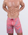 Frontal view of a male model wearing the FAST LINES (RAPID RED) Flex Boardshorts for men by DC2 Miami. These stylish boardshorts feature a bold red and white vertical stripe pattern, a dual-type "hybrid" waistband with a flat front and elasticated back, and a long-leg cut, perfect for beach days and summer adventures.