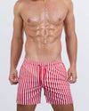 Frontal view of a male model wearing the FAST LINES (RAPID RED) Resort Shorts for men by DC2 Miami. These above-the-knee swim shorts feature a striking red and white striped pattern, an elastic waistband with an adjustable drawstring, and a relaxed fit, making them the perfect choice for beach days.