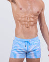 Model wearing FAST LINES (SKY BLUE) poolside shorts featuring a vertical striped print in crisp blue and white. Modern swimwear with a sporty fit and adjustable drawstring.