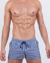Model wearing FAST LINES (NAVY BLUE) poolside shorts in a bold navy and white vertical stripe print. Modern resortwear designed for standout beachside moments with quad-accentuating fit and metallic drawcord tips.