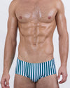 Model wearing FAST LINES (PACIFIC GREEN) men's swim sunga with deep green and white vertical stripes. A modern twist on the classic Brazilian swimwear silhouette offering bold contrast and confident energy.