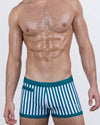 Model wearing FAST LINES (PACIFIC GREEN) men's swim trunks in green and white vertical stripes. Square-cut swimwear with contour-fit design, low-rise waistband, and signature DC2 Miami logo—perfect for beach, resort, or poolside style.