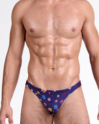 DC2 Flower Powers (Blue) Swim Thong — model wearing deep navy swim thong with vibrant multicolor floral print and minimal low-rise silhouette.