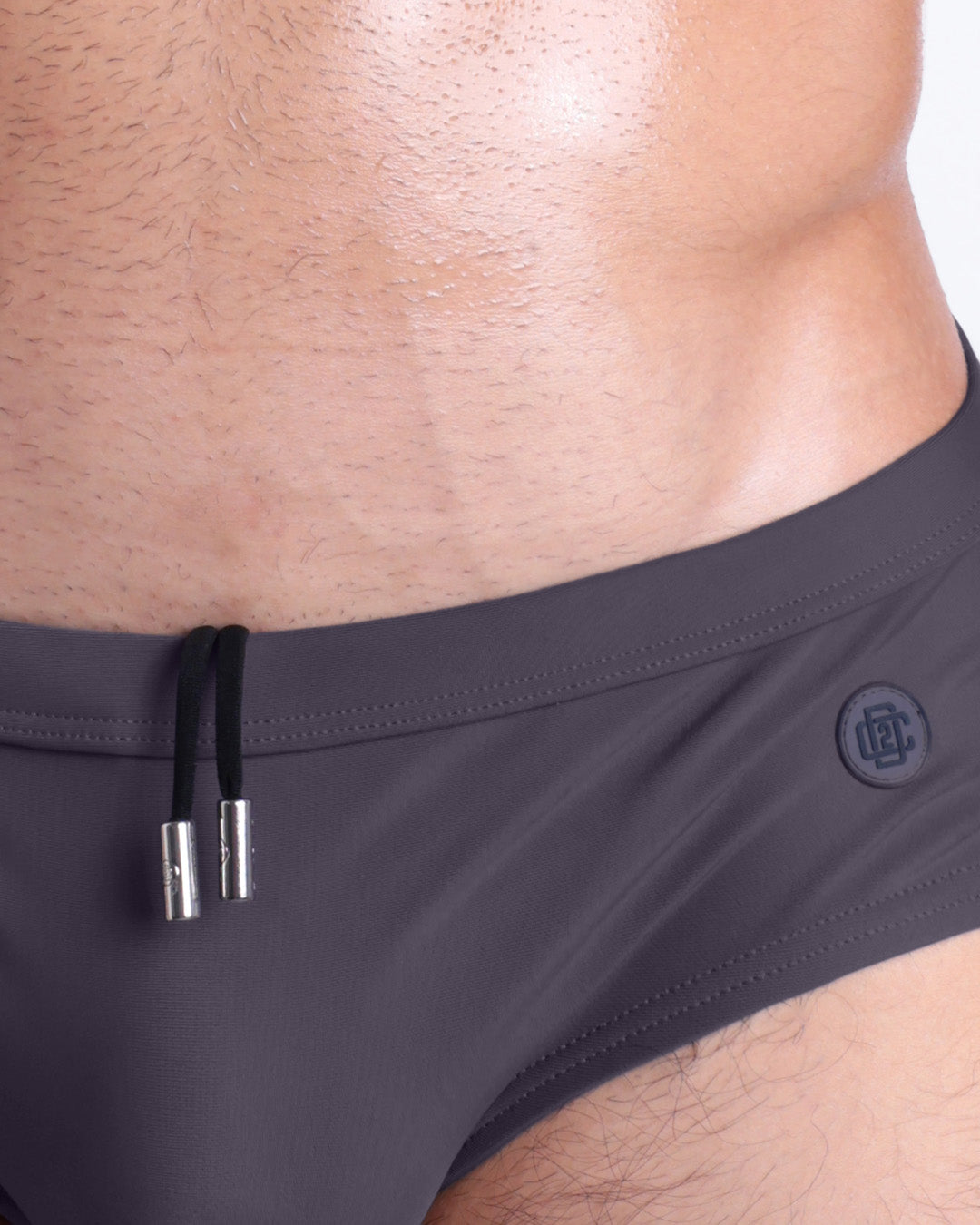 Close-up view of the GOTHAM GREY men’s drawstring briefs showing black cord with custom branded metallic silver cord ends, and matching custom eyelet trims in silver.