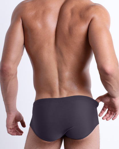 Back view of a male model wearing the GOTHAM GREY beach Brazilian Sunga swimwear for men by DC2 Miami in a solid smoke-gray color.