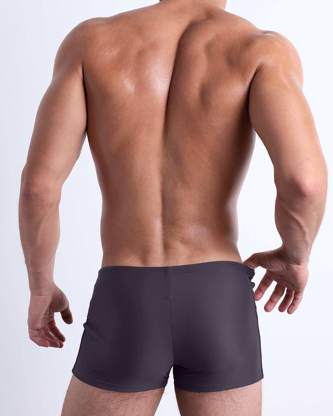 Back view of a male model wearing the GOTHAM GREY men’s swim trunks by BANG! Miami in a solid smoke-grey color.