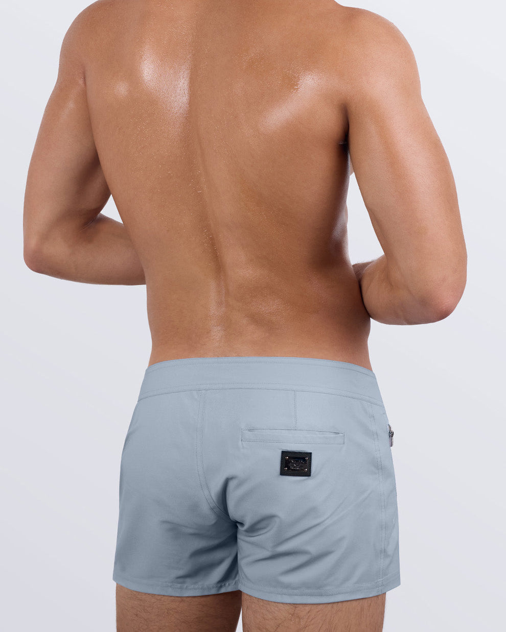 Back view of a male model wearing stone grey men's beach trunks by DC2 Miami a premium men's beachwear brand. Featuring a sleek fit and modern design, these versatile swim trunks combine style and functionality for the perfect beach or poolside look.