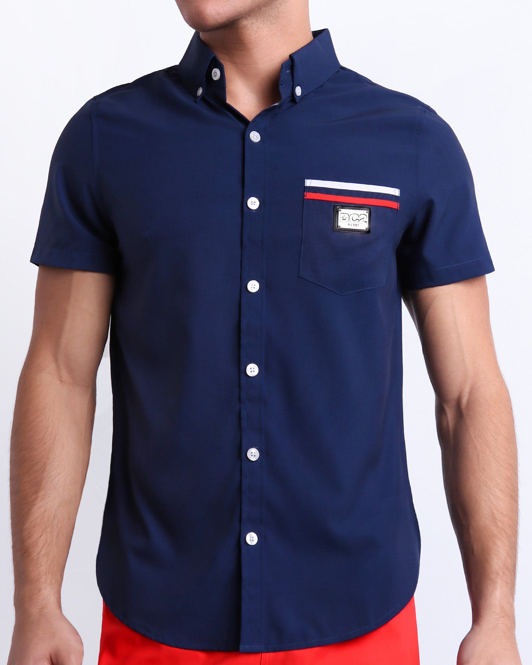 Male model wearing IMPERIAL BLUE men’s sleeveless stretch shirt. A premium quality top in a solid navy blue color with red and white stripes on the pocket, a men’s beachwear brand from Miami.