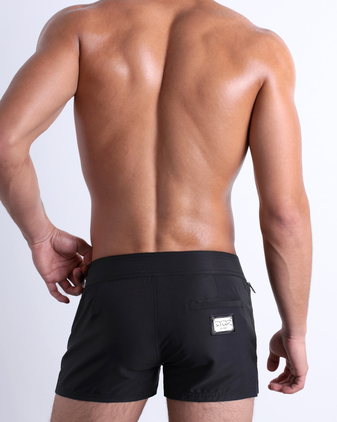 View of a male model wearing the men’s JET BLACK Beach Shorts, in a black color for men. These premium quality swimwear bottoms are by DC2 a capsule brand from BANG! Clothes, a men’s beachwear brand from Miami.