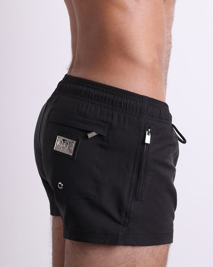 Side view of the JET BLACK swimsuit Poolside Shorts men’s shorter length shorts with side zipper pockets featuring a dark black color. These high-quality swimwear bottoms by DC2, a men’s beachwear brand from Miami.