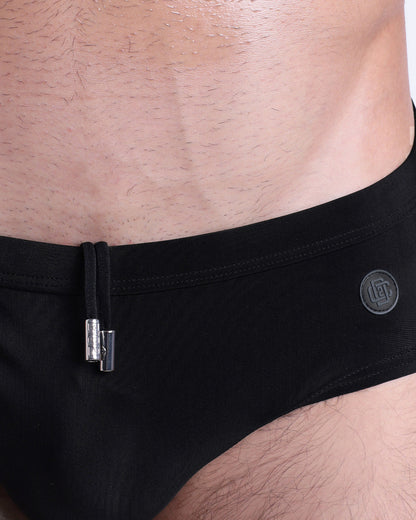 Close-up view of the JET BLACK men’s drawstring briefs showing black cord with custom branded metallic silver cord ends, and matching custom eyelet trims in silver.