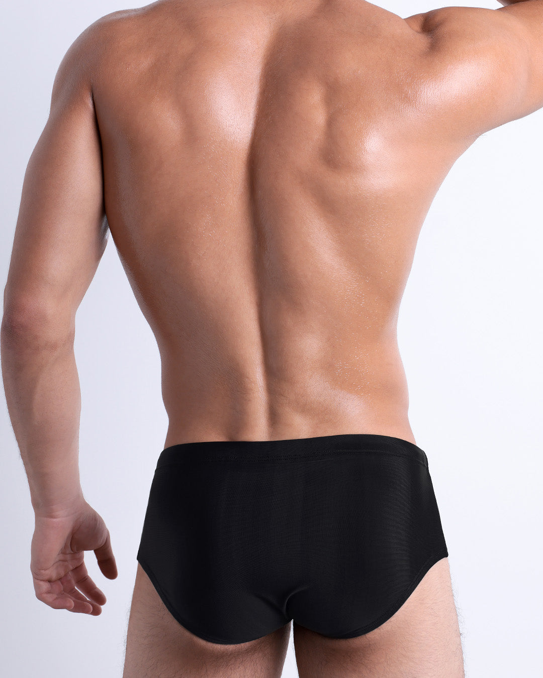 Back view of a male model wearing the JET BLACK men’s Brazilian Sunga swimwear by DC2 Miami in a solid black color.