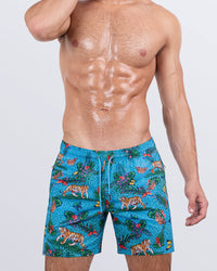 Frontal view of a male model wearing the JUNGLE BOOGIE Resort Shorts for men by DC2 Miami. These above-the-knee swim shorts feature a vibrant jungle-inspired print with tigers, tropical flora, and a blue leopard pattern. Designed with an elastic waistband, adjustable drawstring, and a relaxed fit, these shorts are ideal for summer getaways, beach parties, and poolside lounging.