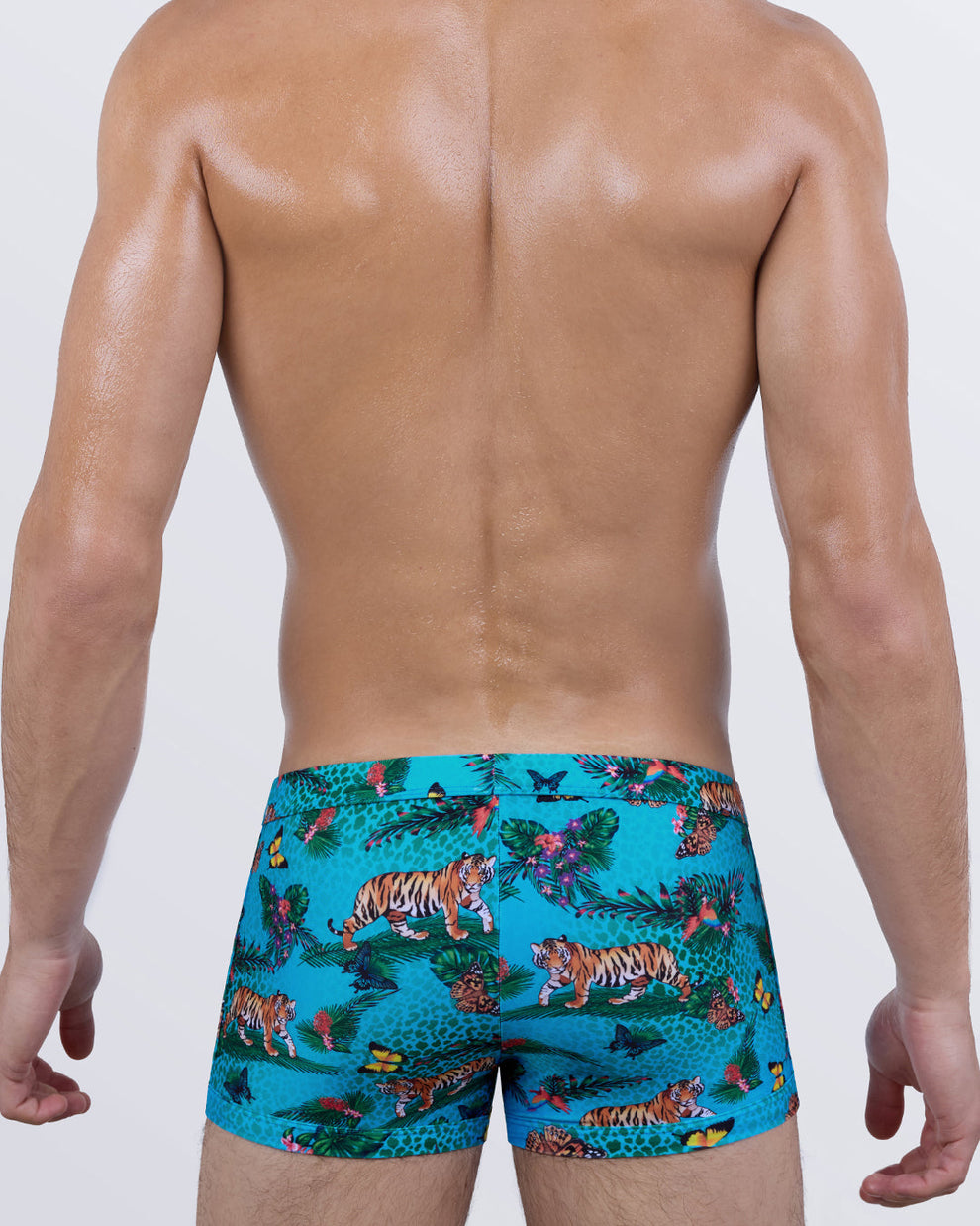 Back view of JUNGLE BOOGIE men's swim trunks showcasing the sculpted rear fit, wide waistband, and all-over tropical jungle pattern in bright turquoise with wild animal and butterfly details.