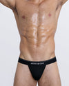 DC2 JUSTIFY MY LOVE Modal Thong — front view on model in black, with bold white waistband text and sleek pouch.