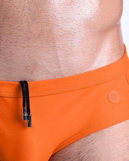 Close-up view of the MATCH POINT ORANGE men’s drawstring briefs showing black cord with custom branded metallic silver cord ends, and matching custom eyelet trims in silver.