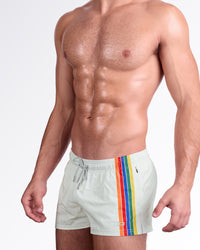 DC2 Sunset Stripes Poolside Shorts — model wearing light sand-colored swim shorts featuring bold rainbow side stripes and an elastic waistband with an adjustable orange drawstring for a vibrant poolside look.