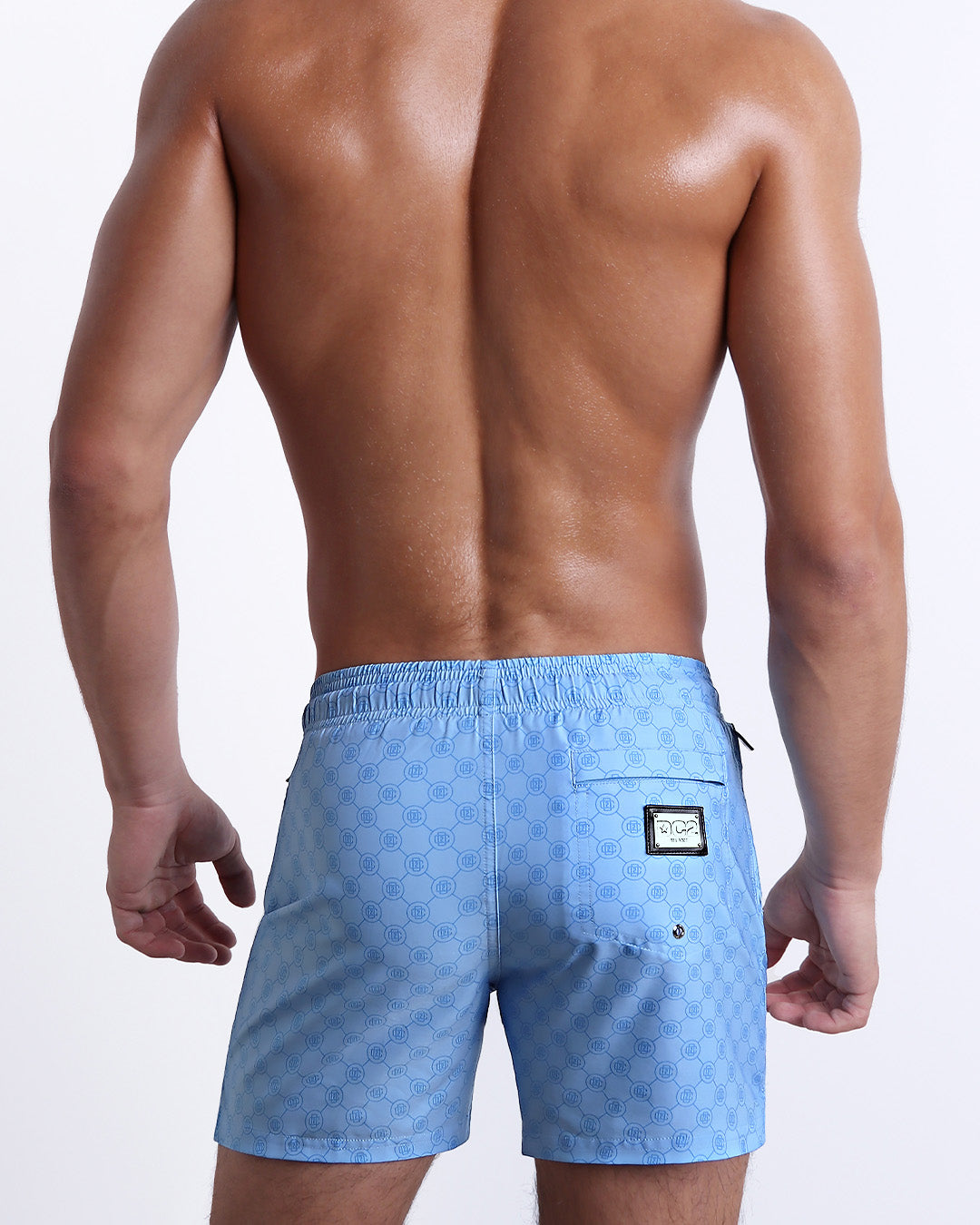 Back view of the MONO BLUE beach Resort Shorts in a light blue color with a darker blue monogram logo, complete with a back pocket, designed by DC2.